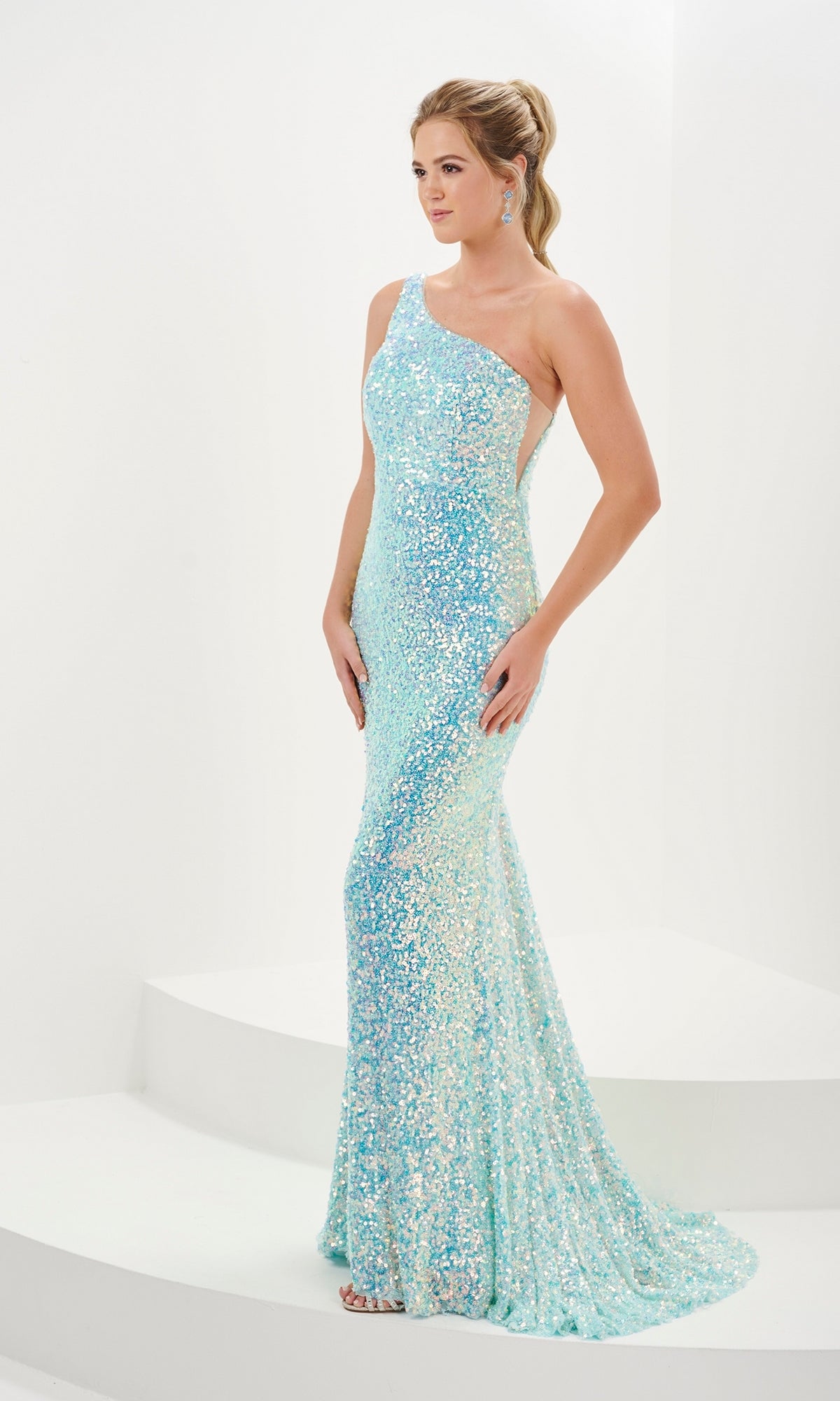 A woman stands on white steps wearing the Tiffany One-Shoulder Long Sequin Prom Dress 16114, featuring a fitted silhouette, sparkling light blue sequins, and a small train.